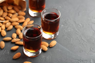 Photo of Glasses with tasty amaretto liqueur and almonds on dark gray table, closeup. Space for text