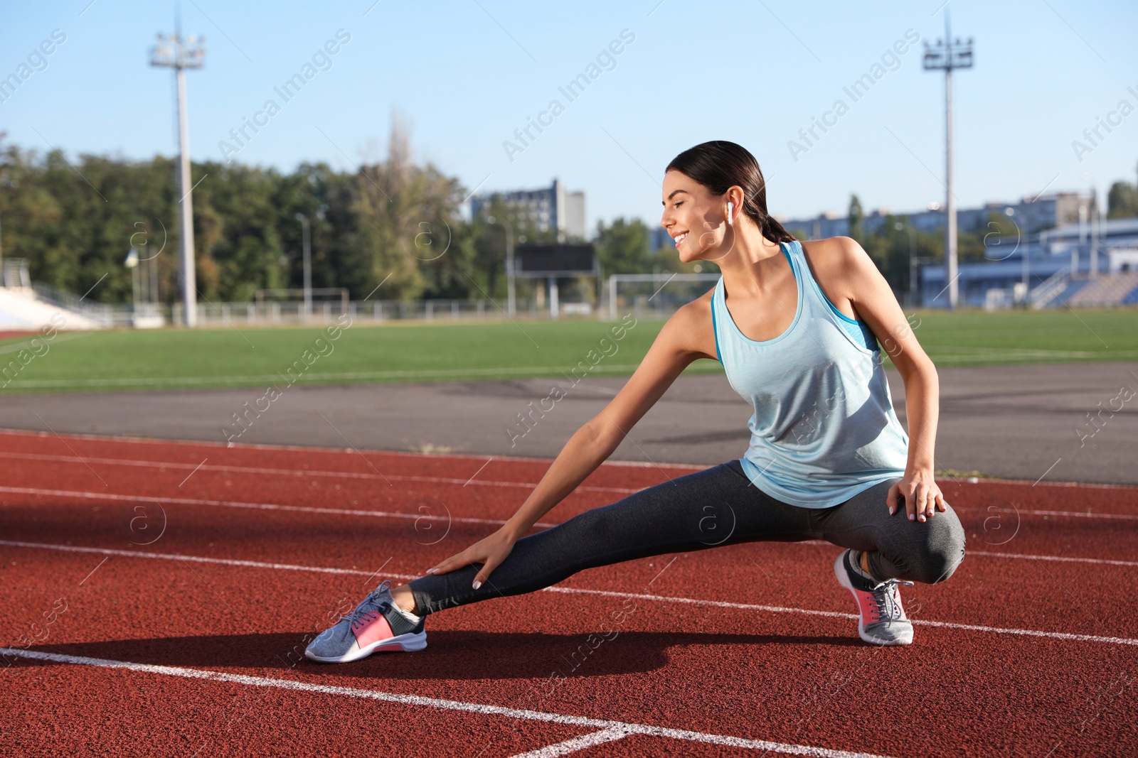 Photo of Young sportswoman with wireless earphones stretching at stadium