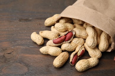 Photo of Paper bag with fresh peanuts on wooden table, closeup. Space for text