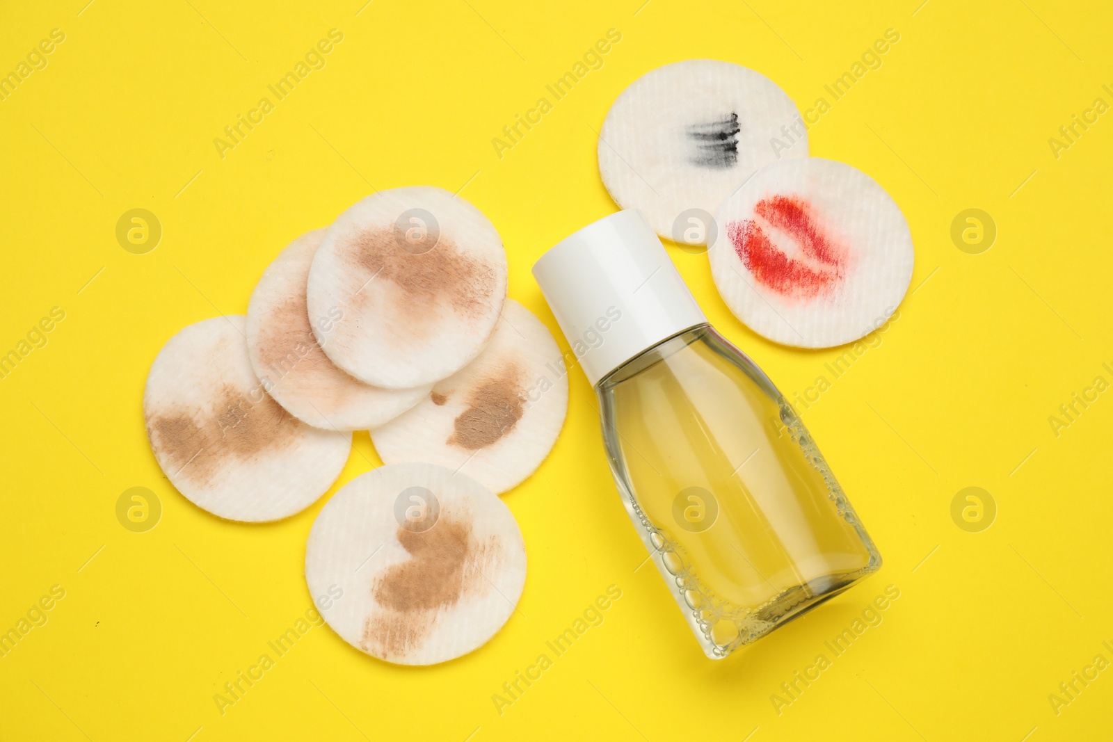 Photo of Bottle of makeup remover and dirty cotton pads on yellow background, flat lay