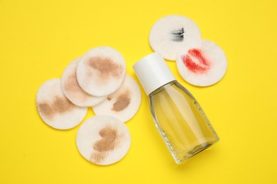 Photo of Bottle of makeup remover and dirty cotton pads on yellow background, flat lay