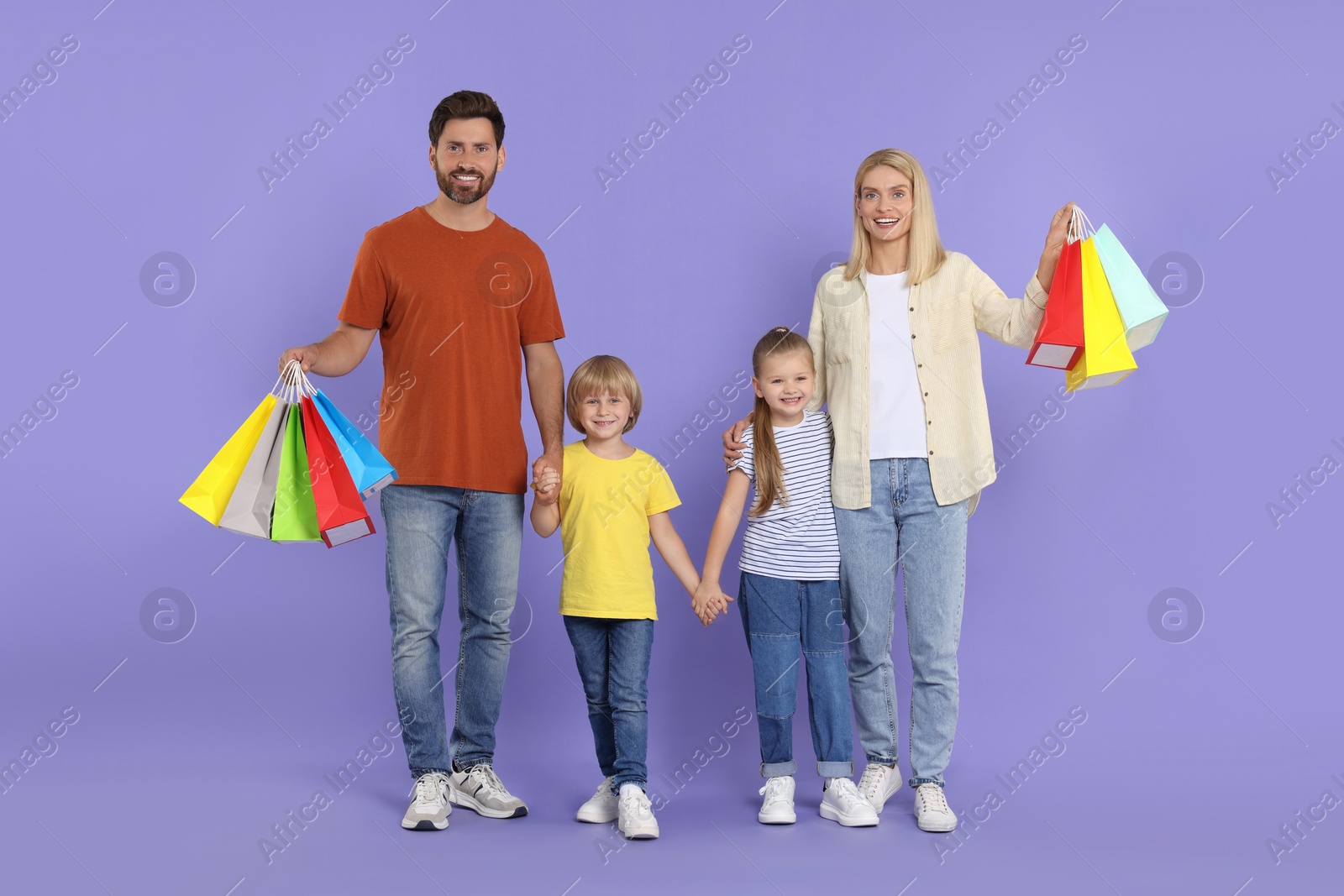 Photo of Family shopping. Happy parents and children with many colorful bags on violet background