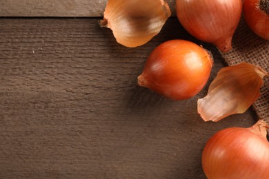 Many ripe onions on wooden table, flat lay. Space for text