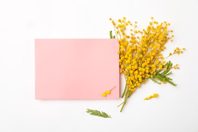 Beautiful mimosa flowers and paper note on white background, flat lay. Space for text