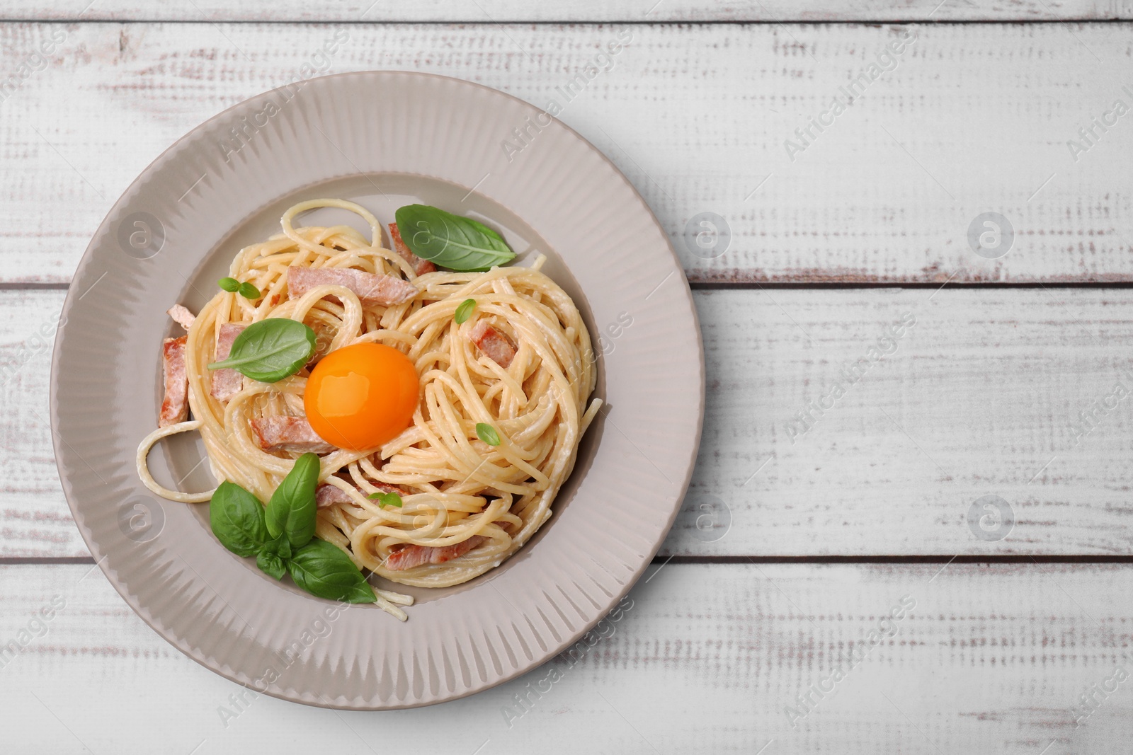 Photo of Delicious pasta Carbonara with egg yolk on white wooden table, top view. Space for text