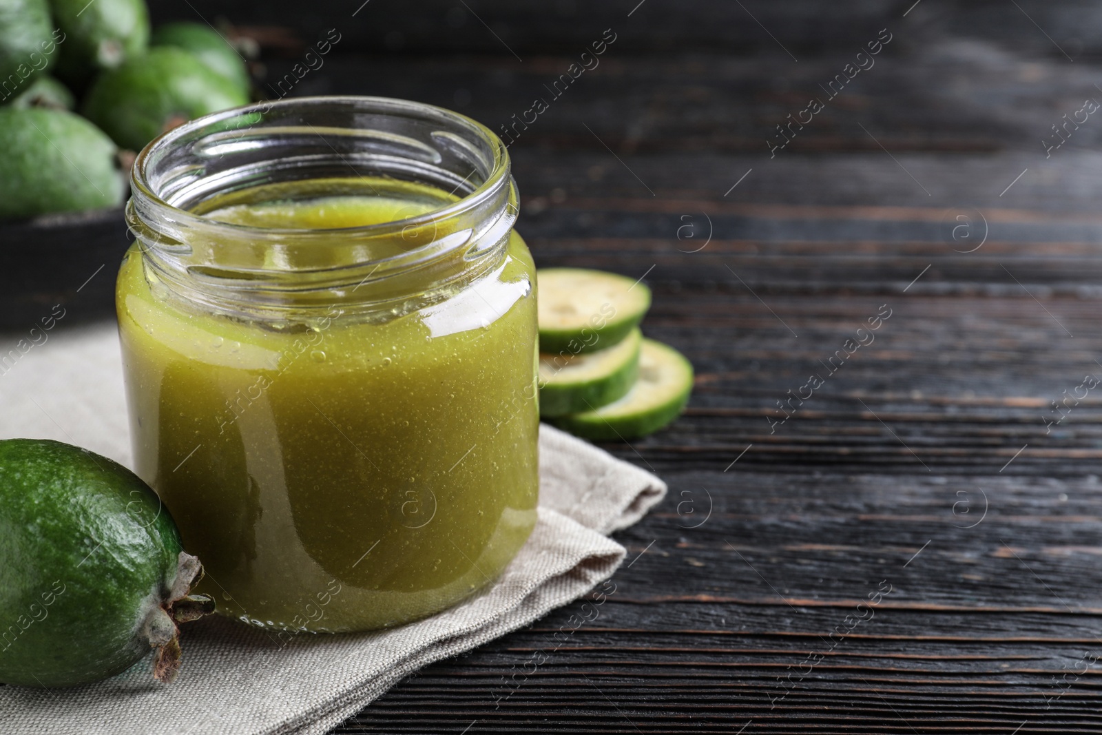 Photo of Feijoa jam and fresh fruit on black wooden table, closeup. Space for text