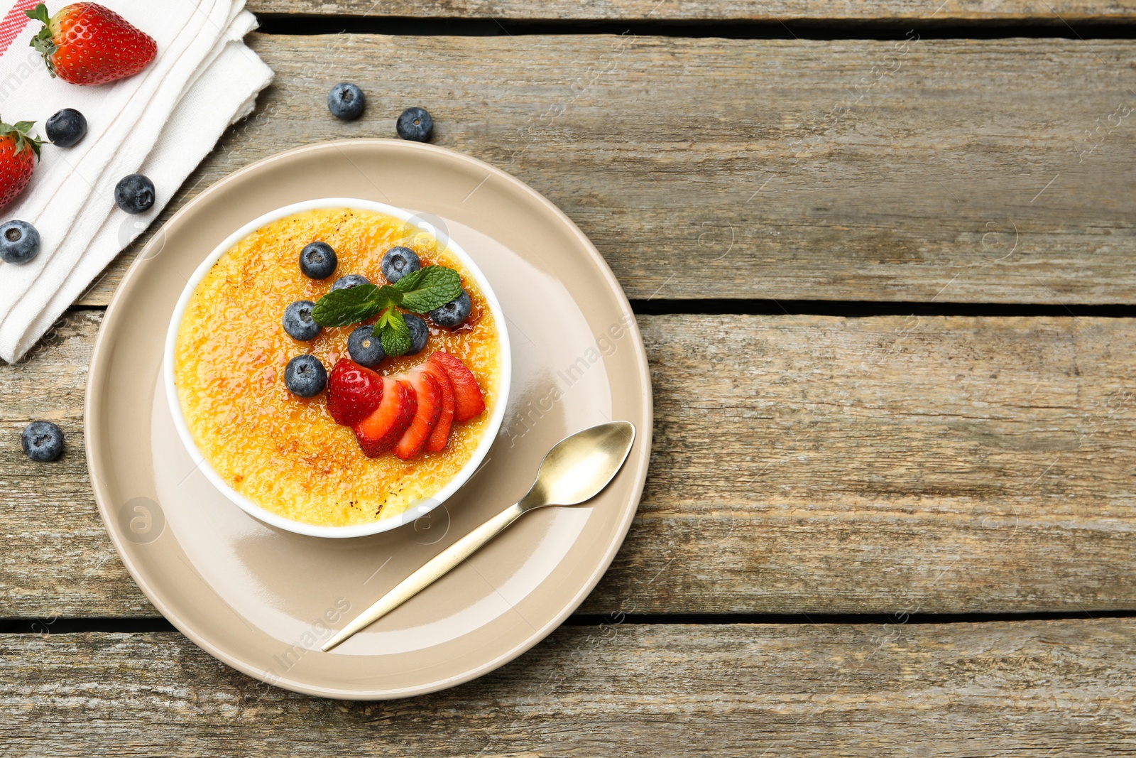 Photo of Delicious creme brulee with berries and mint in bowl on wooden table, top view. Space for text