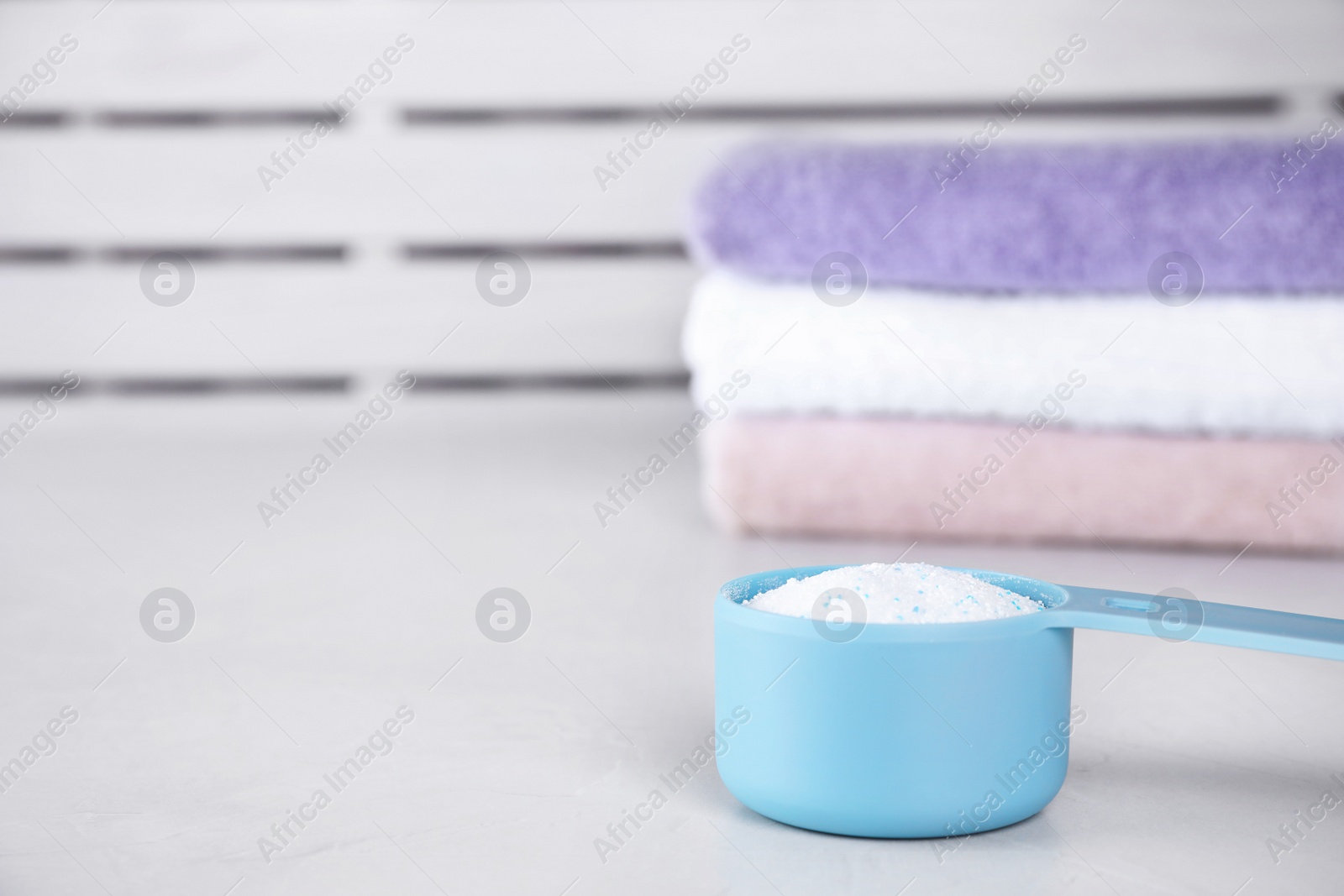 Photo of Clean towels and measuring scoop of washing powder on table. Space for text