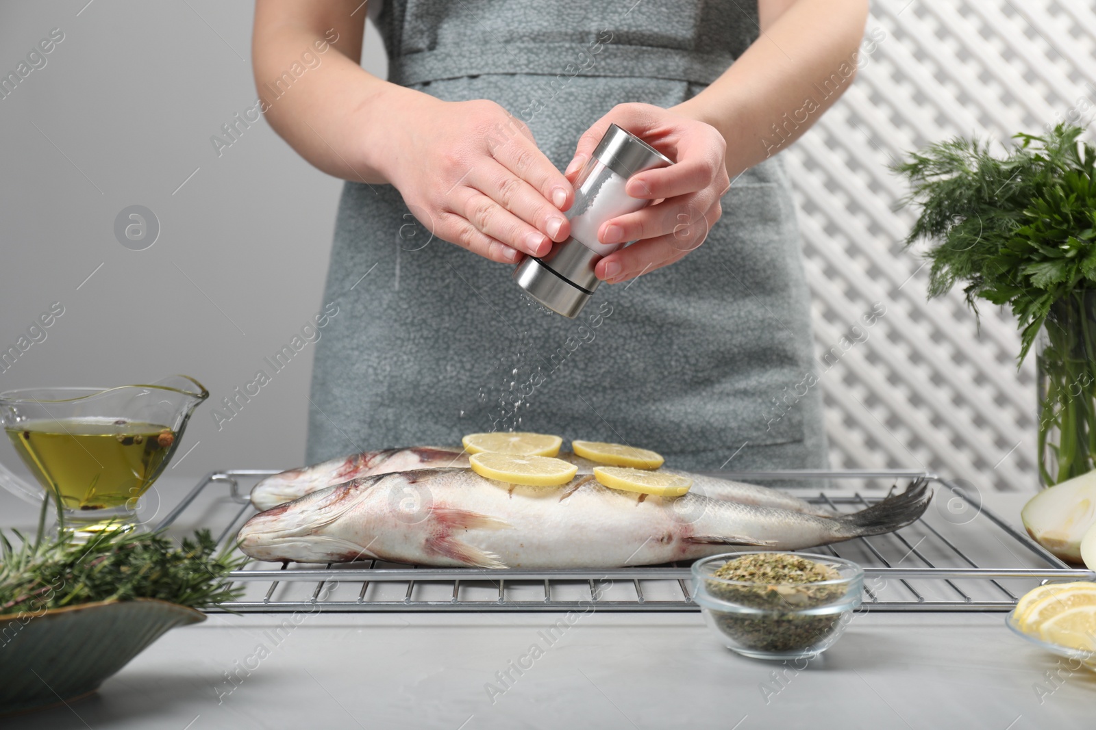 Photo of Woman salting raw sea bass fish with lemon at table, closeup