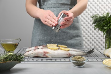 Woman salting raw sea bass fish with lemon at table, closeup