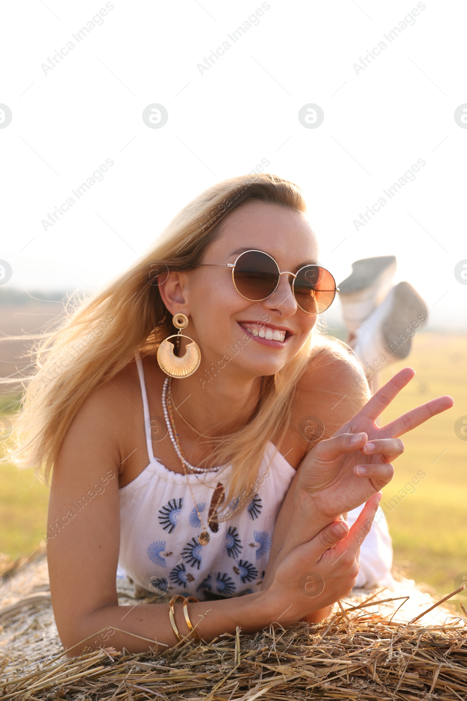 Photo of Beautiful hippie woman showing peace sign on hay bale in field