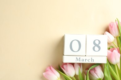 Photo of Wooden block calendar with date 8th of March and tulips on beige background, flat lay. Space for text