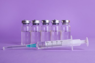 Disposable syringe with needle and vials on violet background