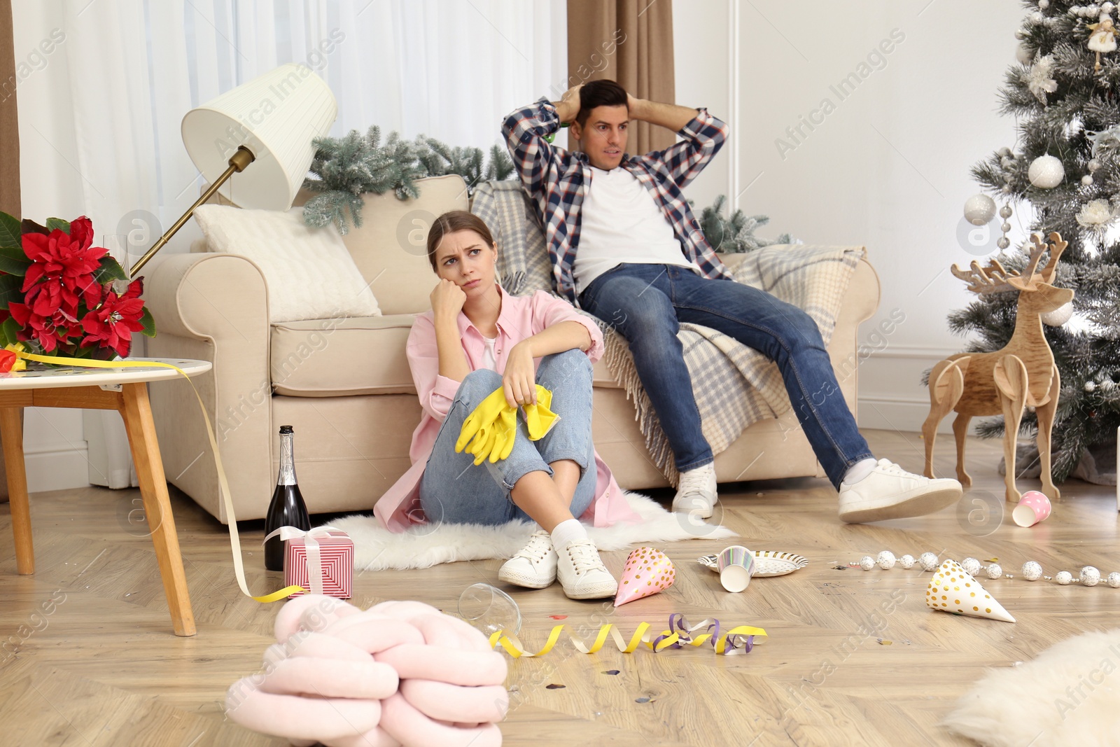 Photo of Tired couple sitting in messy room while cleaning after New Year party