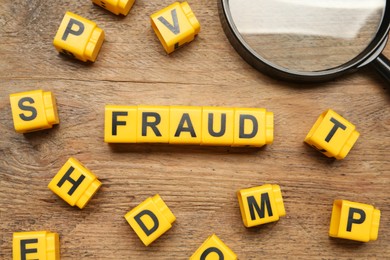 Word Fraud of yellow cubes with letters and magnifying glass on  wooden background, flat lay