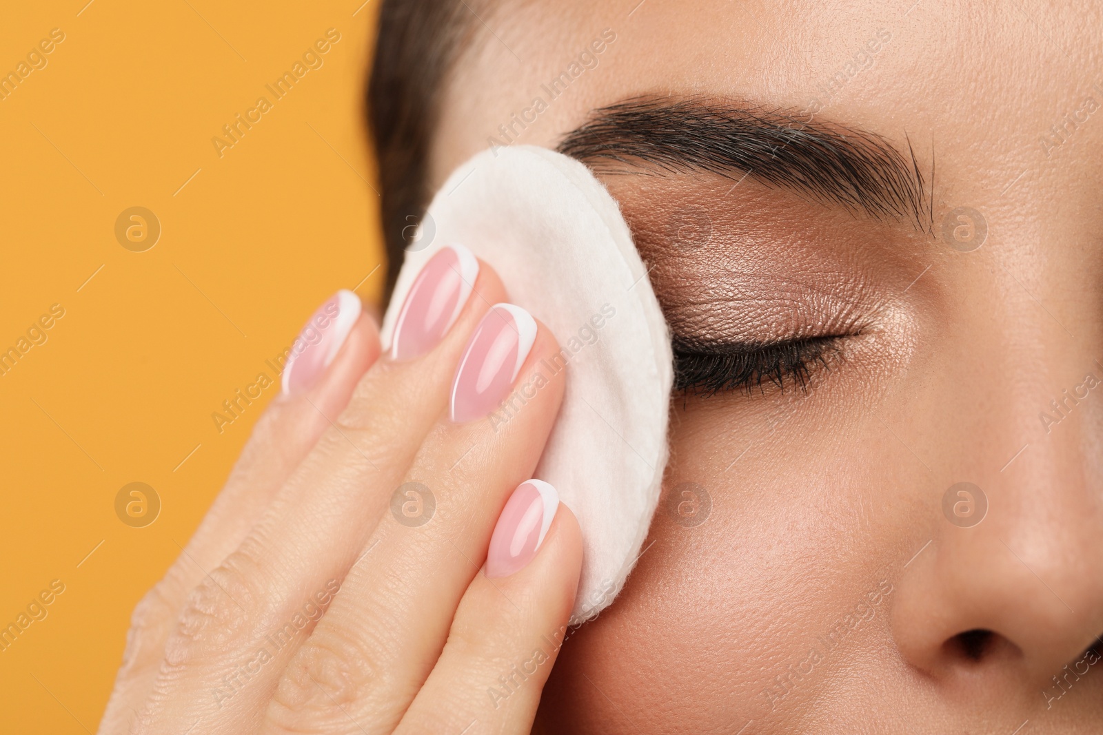 Photo of Beautiful woman removing makeup with cotton pad on orange background, closeup. Space for text