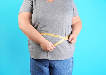 Overweight woman measuring waist before weight loss on color background