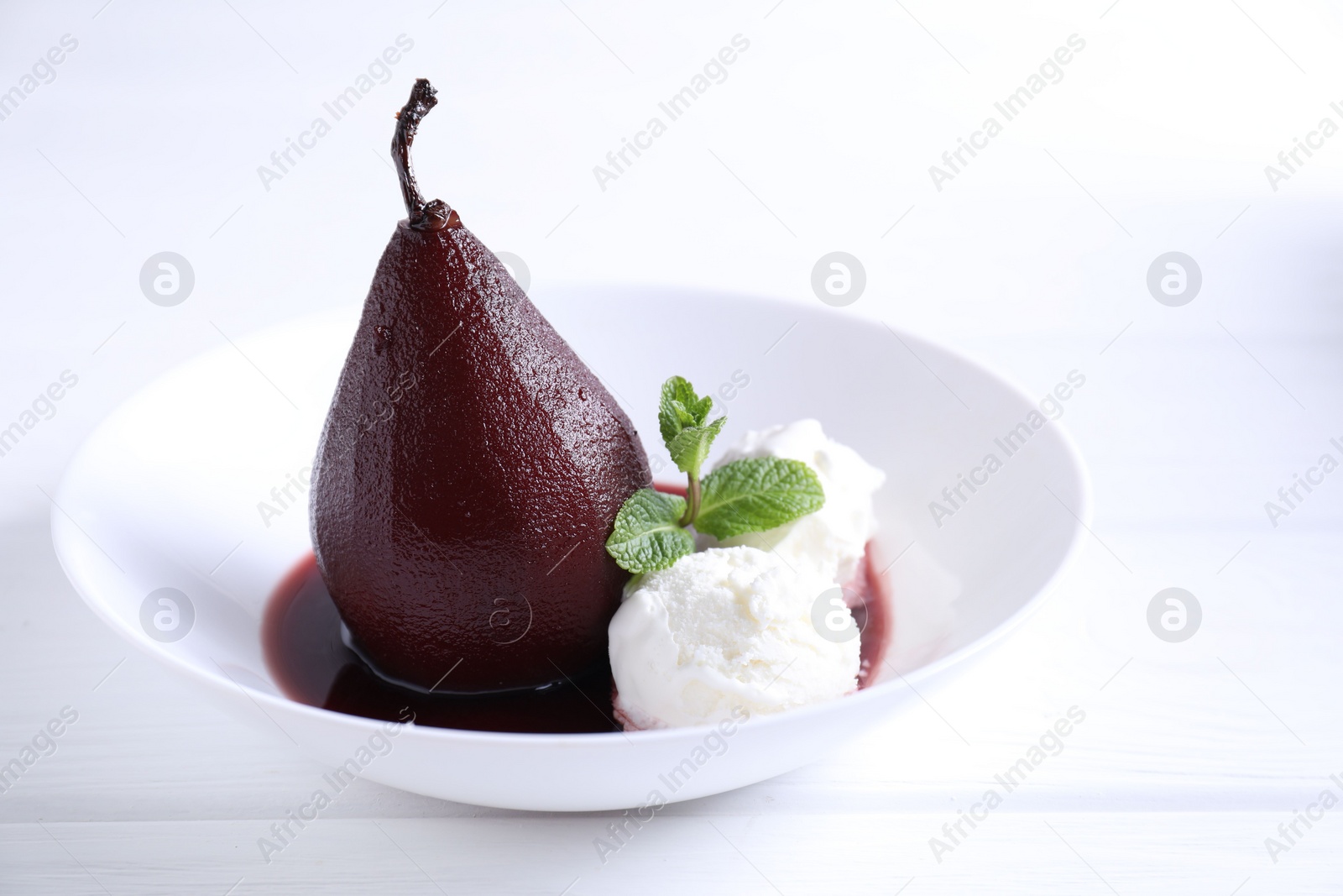 Photo of Tasty red wine poached pear with mint and Ice cream on white wooden table, closeup