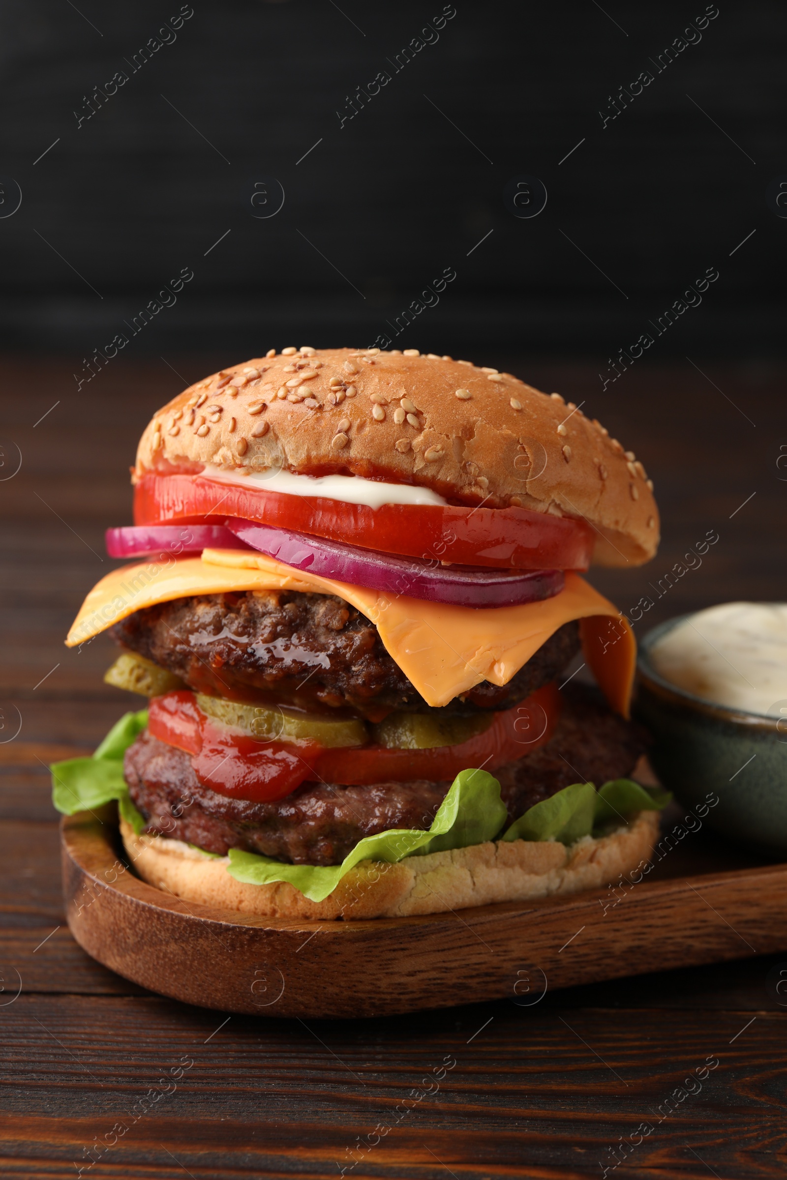 Photo of Tasty cheeseburger with patties and sauce on wooden table, closeup