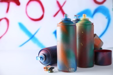 Many spray paint cans near white wall with different drawn symbols, space for text