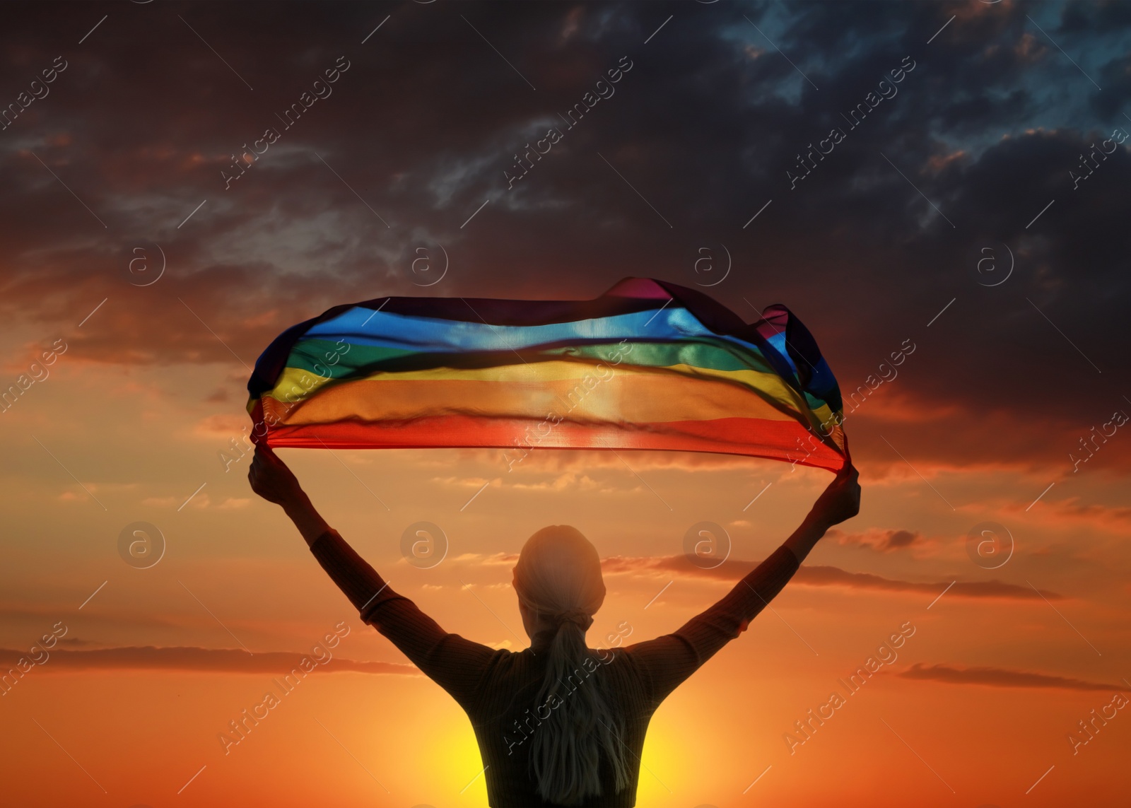 Image of Woman with bright LGBT flag against sky at sunset