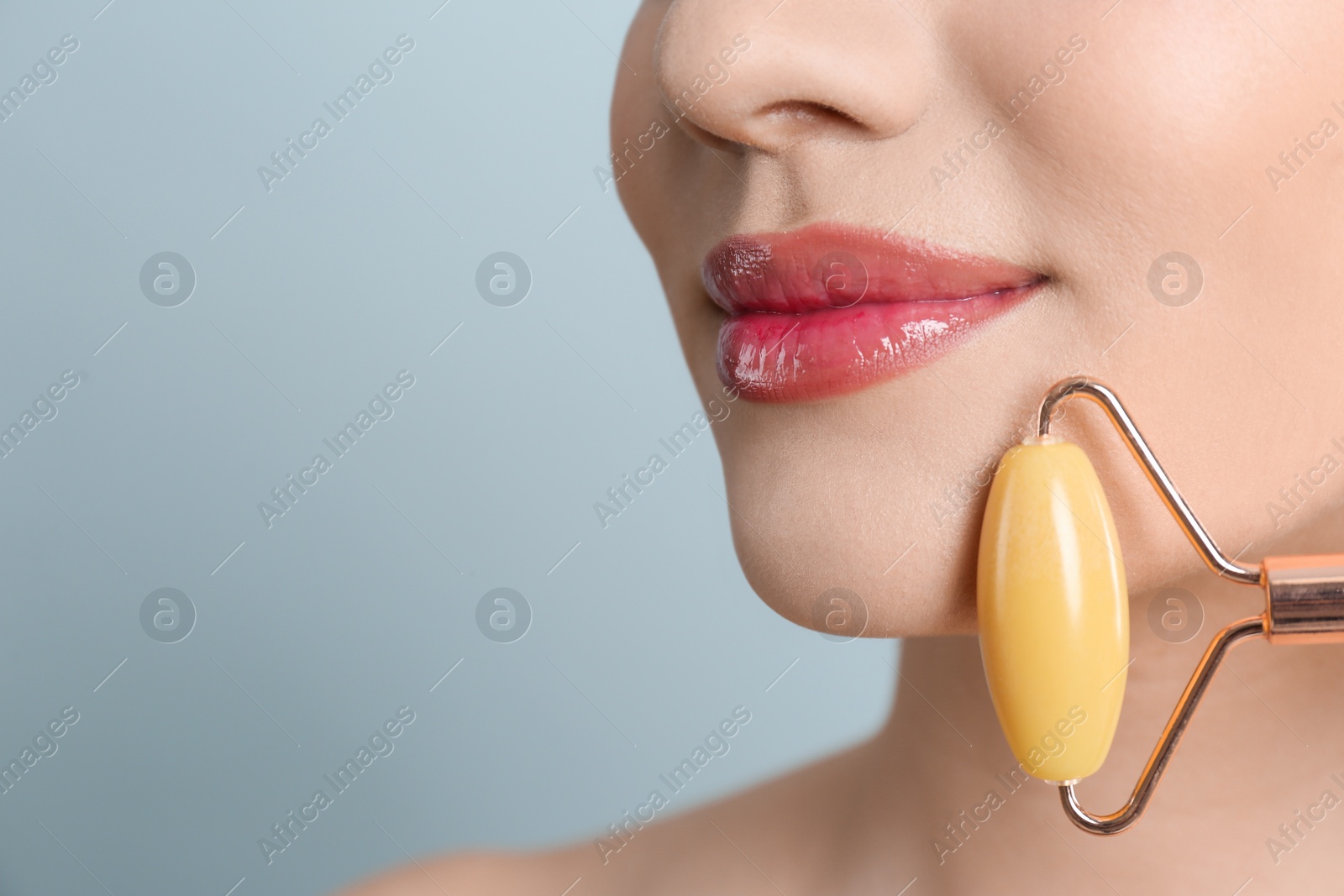 Photo of Woman using natural jade face roller on grey background, closeup. Space for text