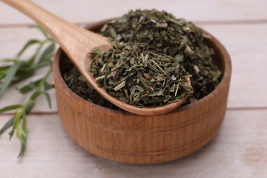 Photo of Bowl of dry tarragon and spoon on wooden table, closeup