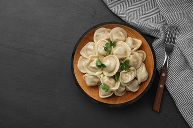 Photo of Tasty dumplings with parsley on black table, flat lay. Space for text