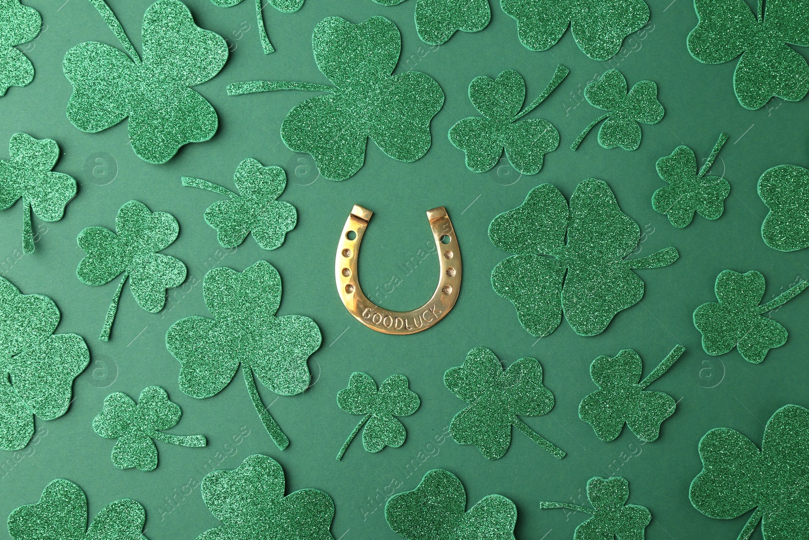 Photo of St. Patrick's day. Golden horseshoe and decorative clover leaves on green background, flat lay