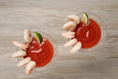 Photo of Tasty shrimp cocktail with sauce and lime in glasses on wooden table, flat lay