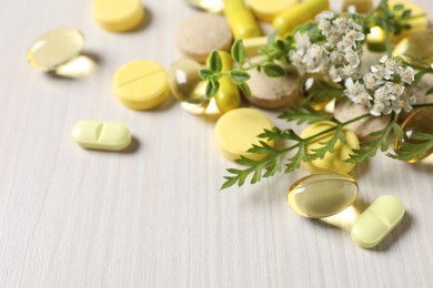 Photo of Different pills, herbs and flowers on white wooden table, closeup with space for text. Dietary supplements