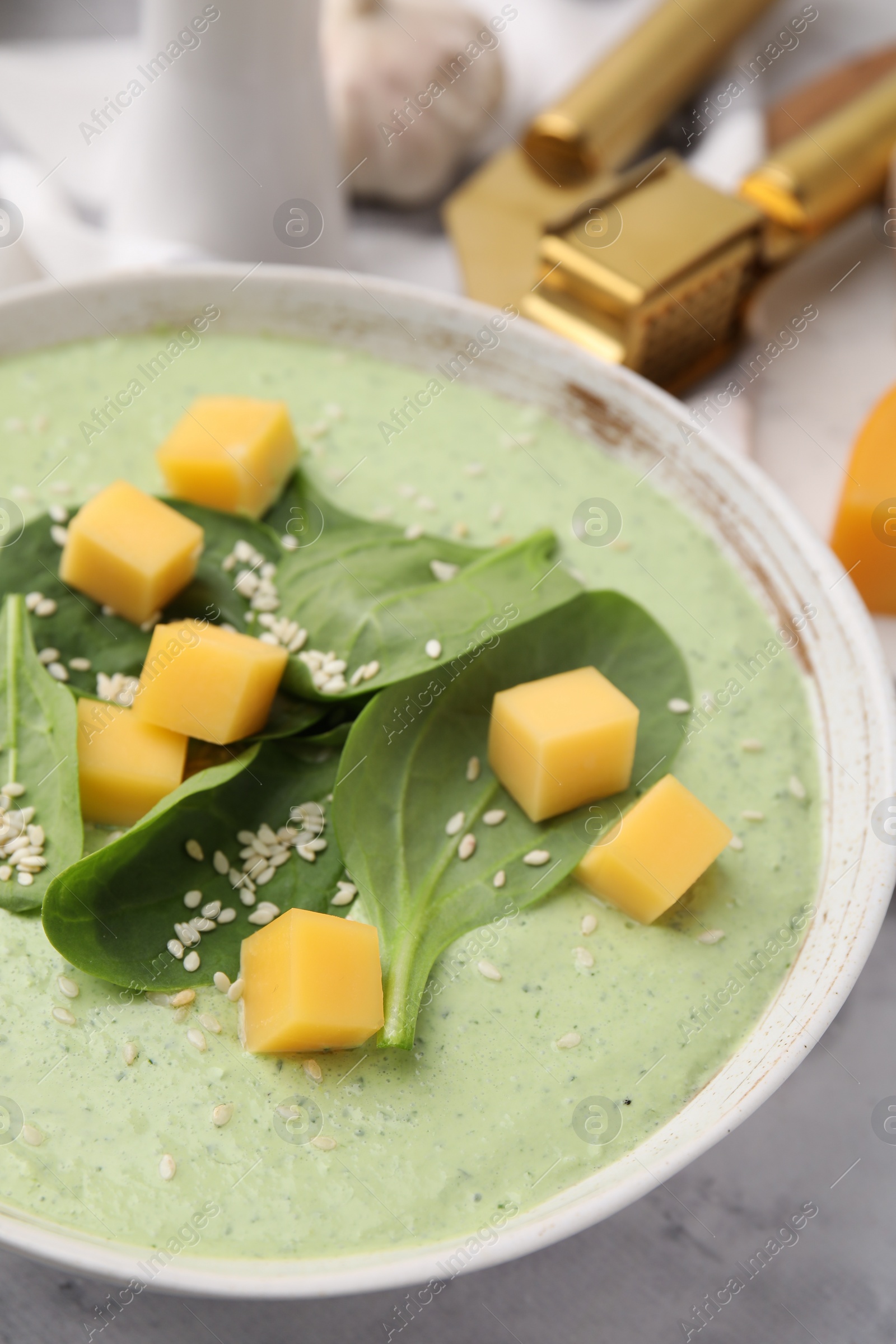 Photo of Delicious spinach cream soup with cheese and sesame seeds in bowl on white marble table