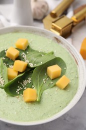 Delicious spinach cream soup with cheese and sesame seeds in bowl on white marble table