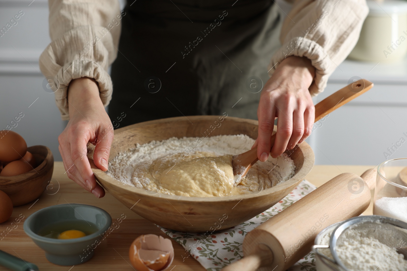 Photo of Woman kneading dough with spoon in bowl at wooden table indoors, closeup