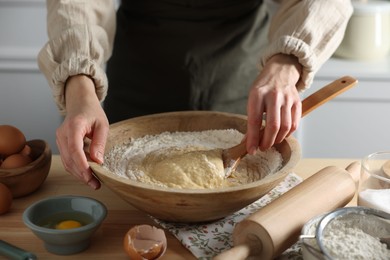 Woman kneading dough with spoon in bowl at wooden table indoors, closeup