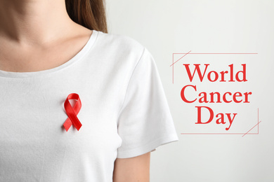 Woman with red ribbon on t-shirt against light background. World Cancer Day