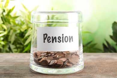 Photo of Glass jar with label PENSION and coins on wooden table