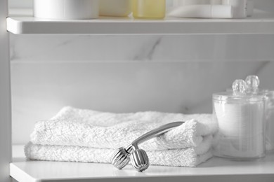 Metal face roller, towels and cotton pads on shelving unit in bathroom