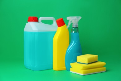 Photo of Different cleaning supplies and sponges on green background