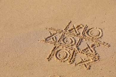 Photo of Tic tac toe game drawn on sandy beach. Space for text