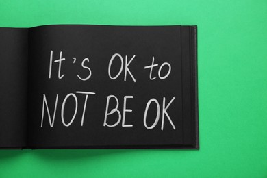 Notebook with phrase It`s Ok To Not Be Ok on green background, top view
