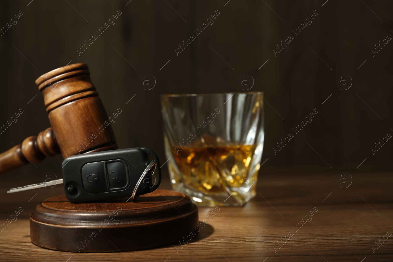 Photo of Car key, gavel near glass of alcohol on wooden table, space for text. Dangerous drinking and driving