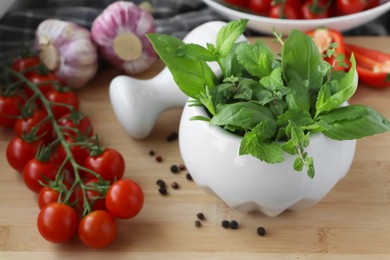 Mortar with different fresh herbs near pepper, garlic and cherry tomatoes on wooden table, closeup