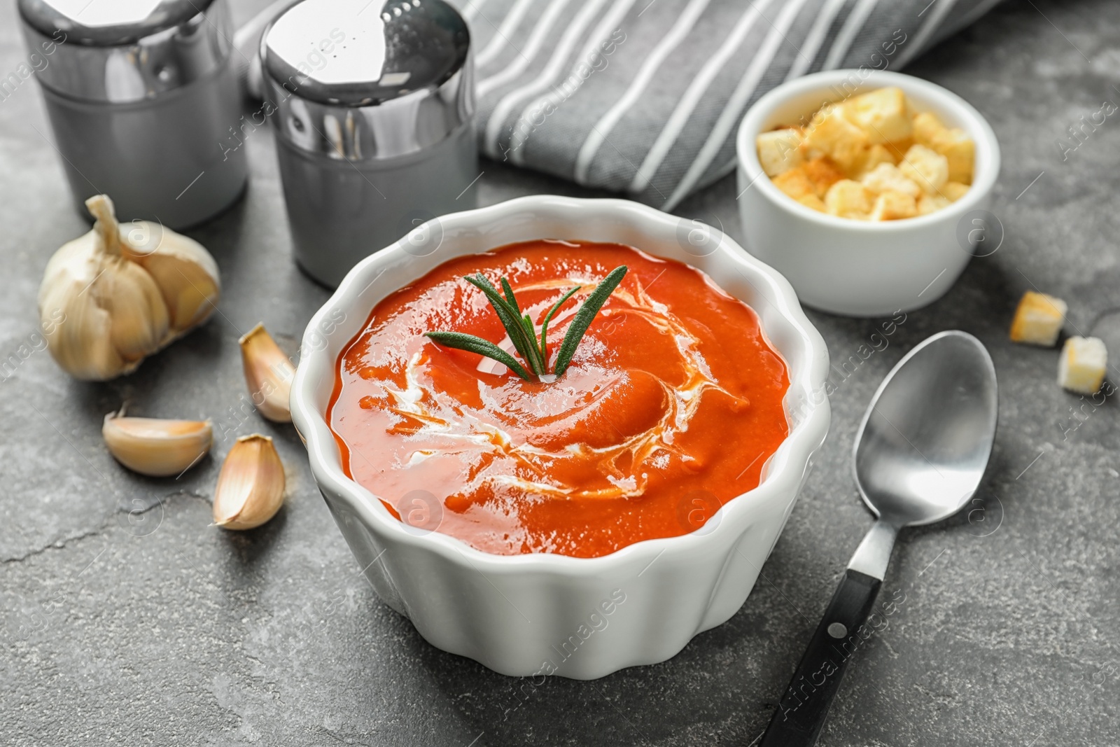 Photo of Fresh homemade tomato soup served with croutons and garlic on grey table