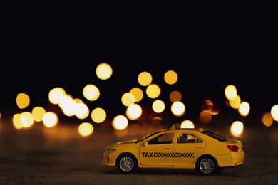 Photo of Yellow taxi car model on table against festive lights. Bokeh effect