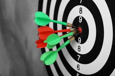 Dart board with arrows hitting target on grey wall, closeup