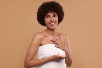 Beautiful young woman applying cream onto body on beige background