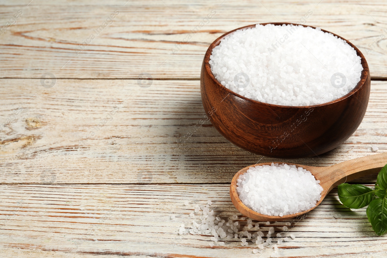 Photo of Bowl and spoon with natural sea salt on white wooden table. Space for text