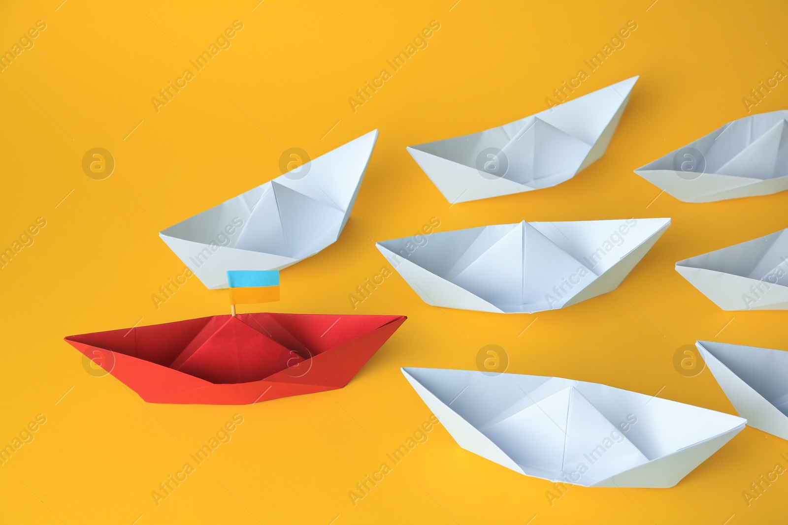 Photo of Group of paper boats following red one on yellow background. Leadership concept