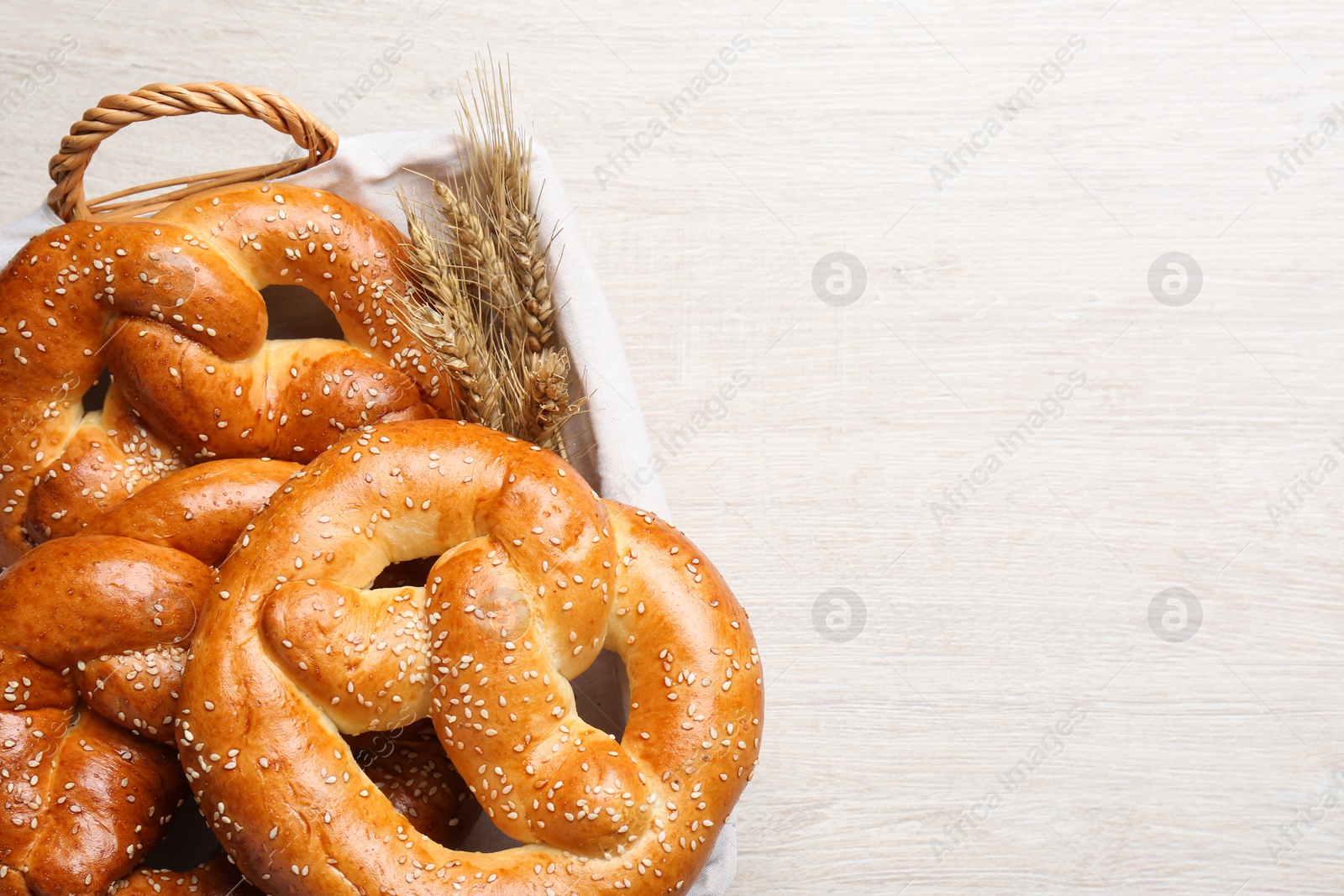 Photo of Basket with delicious pretzels and wheat spikes on white wooden table, top view. Space for text